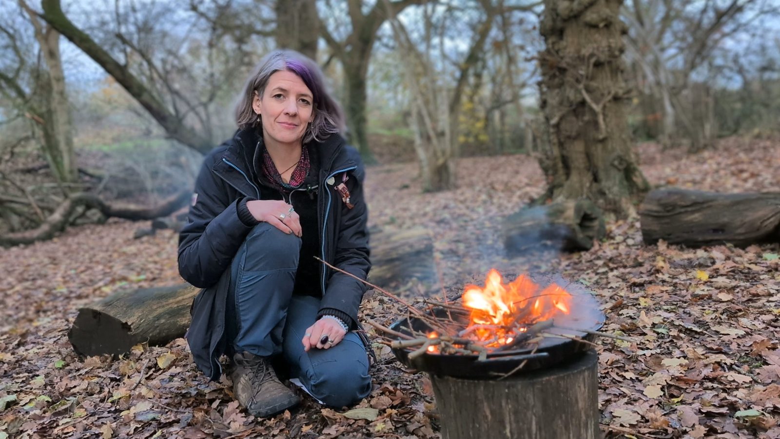 Sarah Allington crouched by a small fire in the woods